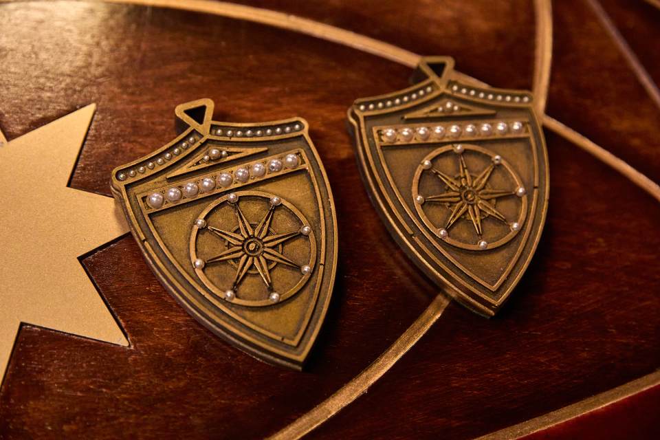Two bronze shield-shaped pendants with pearl accents.