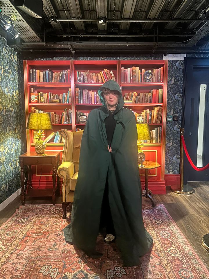 Person in a green cloak standing in a room with bookshelves.