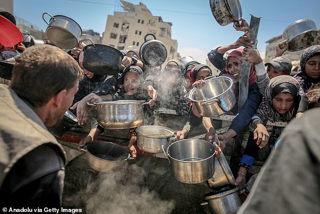 Palestinians, who face difficulties accessing food due to the blockade imposed by Israel, wait to receive hot meals in Gaza