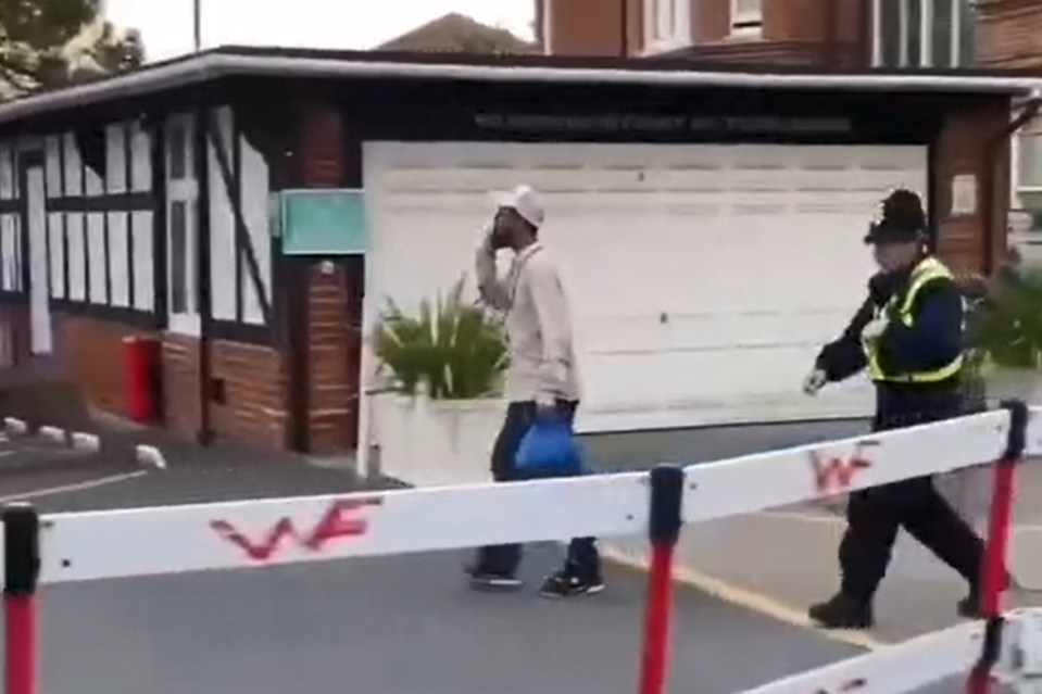 An asylum seeker escorted by a police officer gives a protester the middle finger.