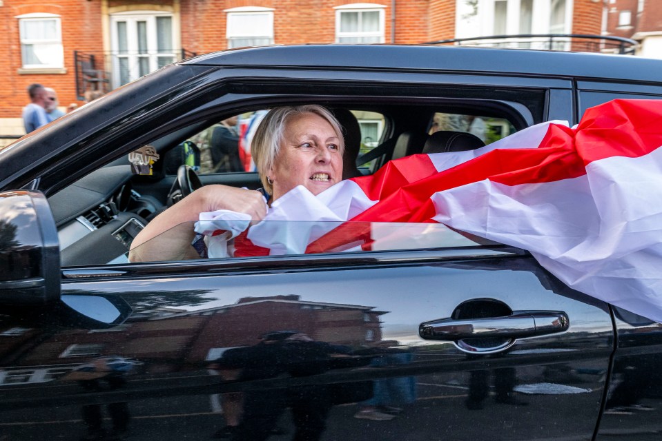 Protestor in car holding English flag during demonstration outside hotel.