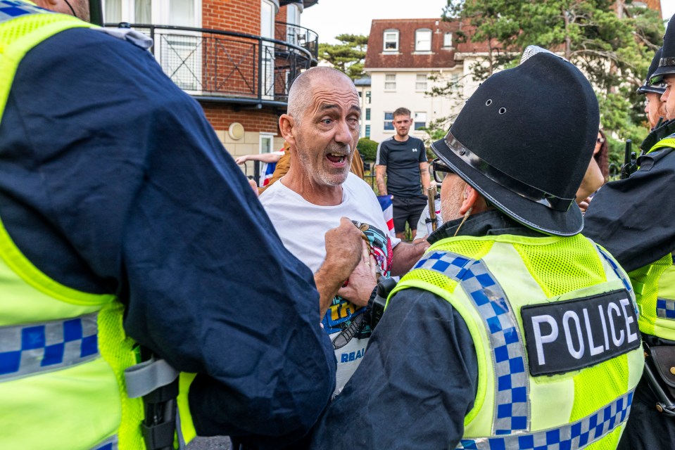 Protestors confronting an asylum seeker escorted by police.