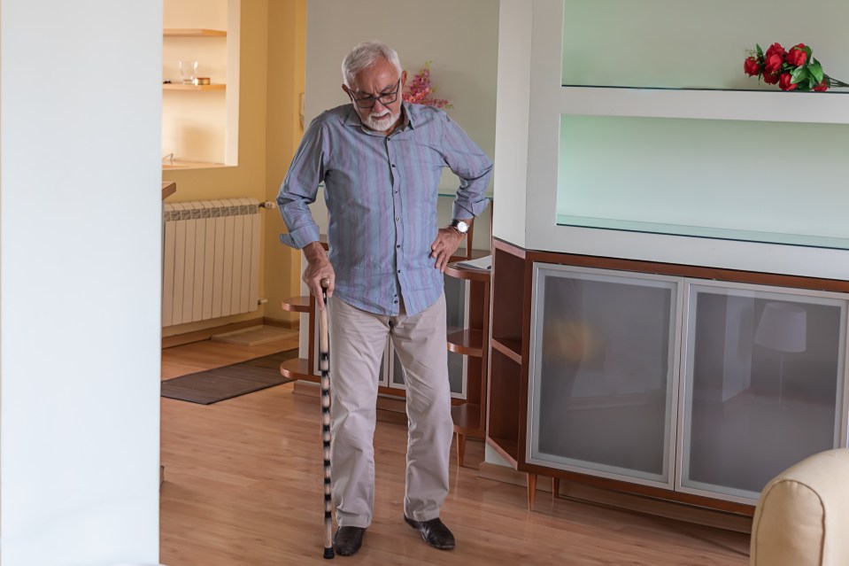 An older man with a cane standing in his living room.