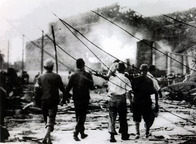 Japanese air raid workers are pictured carrying a victim of the Hiroshima atom bomb away from smoking ruins