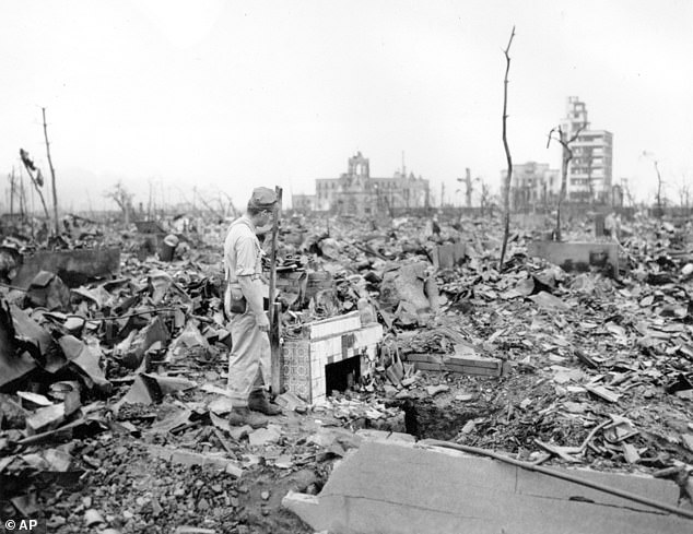 A man stands next to the remains of a tiled fireplace in Hiroshima on a spot that would once have been inside someone's home