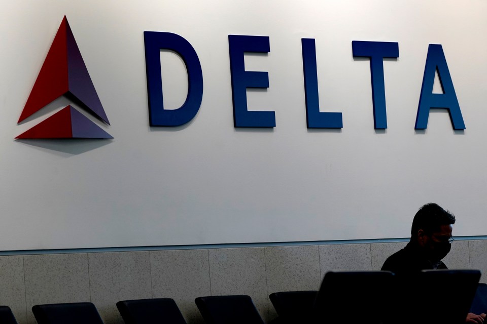 A man wearing a mask waits at a Delta Airlines gate.