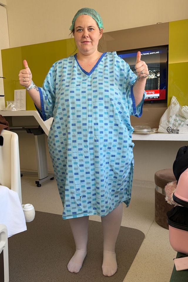 Woman in a hospital gown giving a thumbs up.