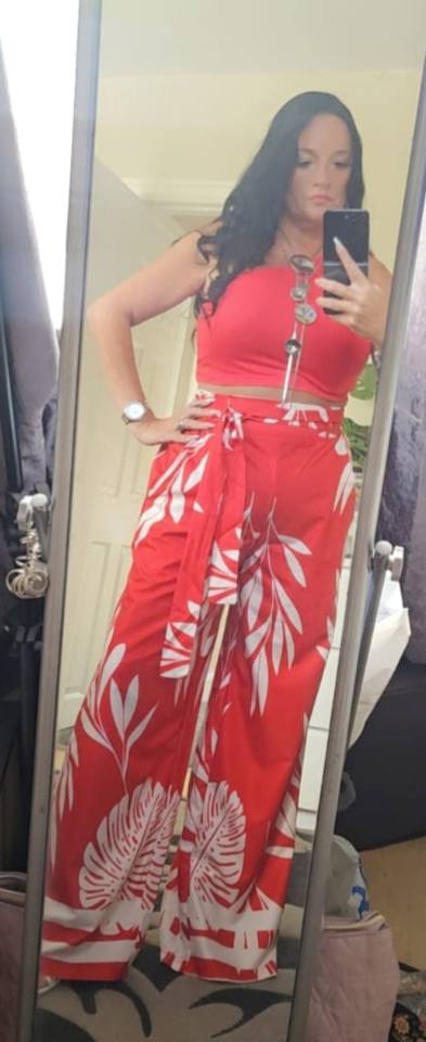 Woman in red leaf-print pants and top taking a selfie.