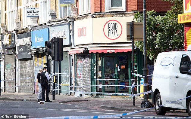 Police officers secure the scene on Denver Road, north London, following the fatal shooting