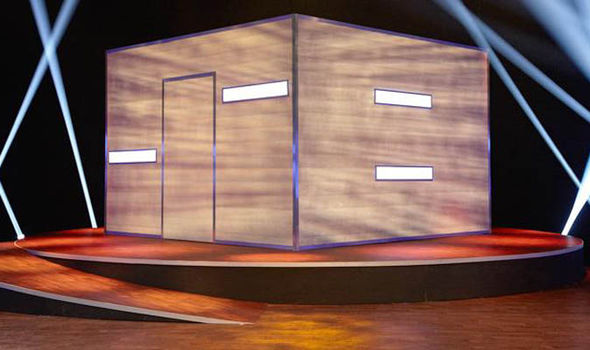 A wooden cube-shaped set piece with a door and blank rectangular panels on a stage.
