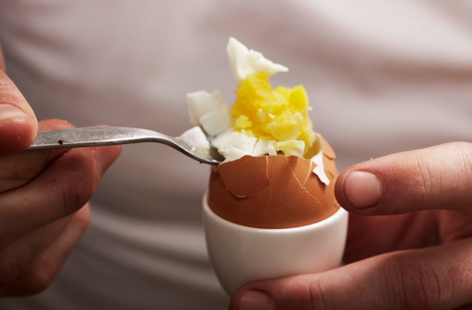 Person eating a hard-boiled egg with a fork.