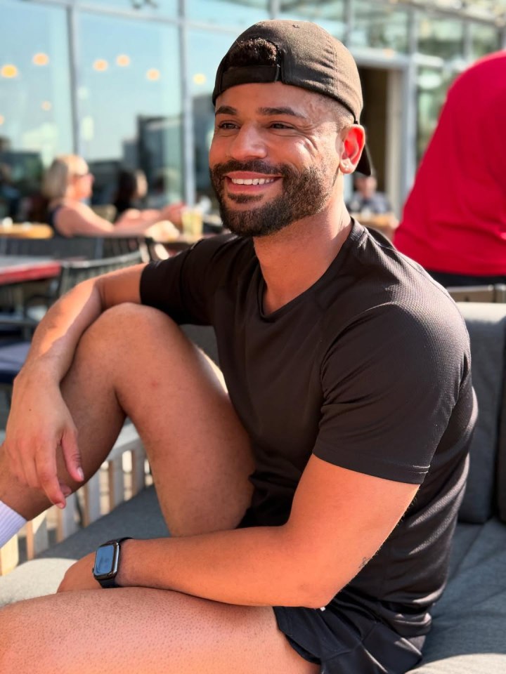Man smiling outdoors while wearing a black shirt and cap.