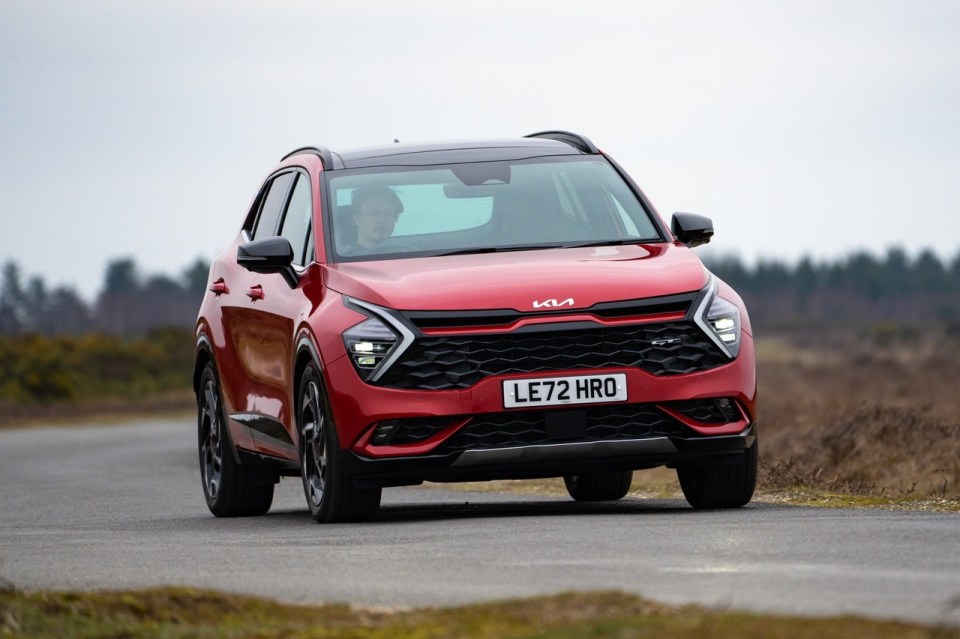 Red Kia Sportage driving on a road.