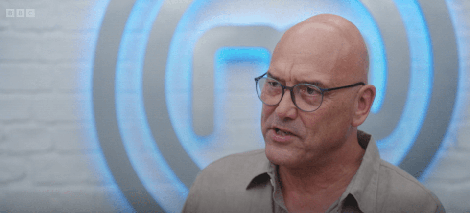 A bald man wearing glasses speaks in front of a MasterChef logo.