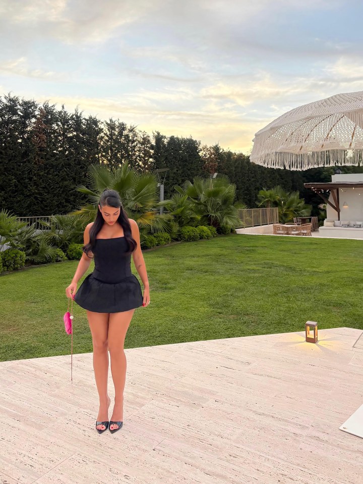 Woman in black dress and heels standing outdoors.