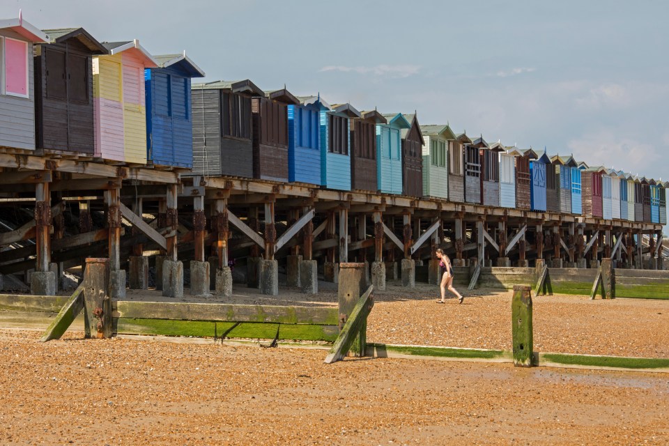 Woman walking on beach past colorful beach huts on stilts.