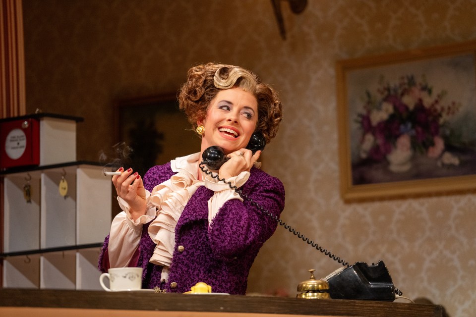 A woman in a purple jacket smokes and talks on a rotary phone.