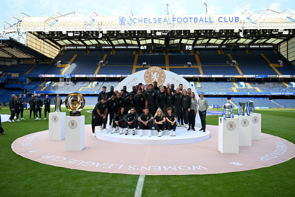 Chelsea men's and women's soccer teams posing with trophies at Stamford Bridge.