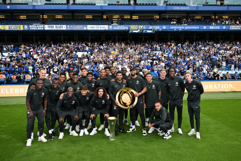 Chelsea men's soccer team posing with trophies in front of cheering fans.