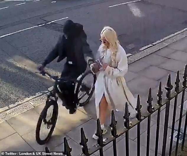 A thief steals a phone from a woman walking down a road in London's exclusive Mayfair area
