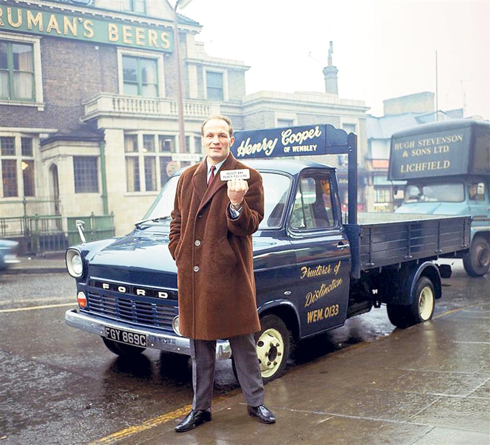 Henry Cooper holding a card, standing by a truck.
