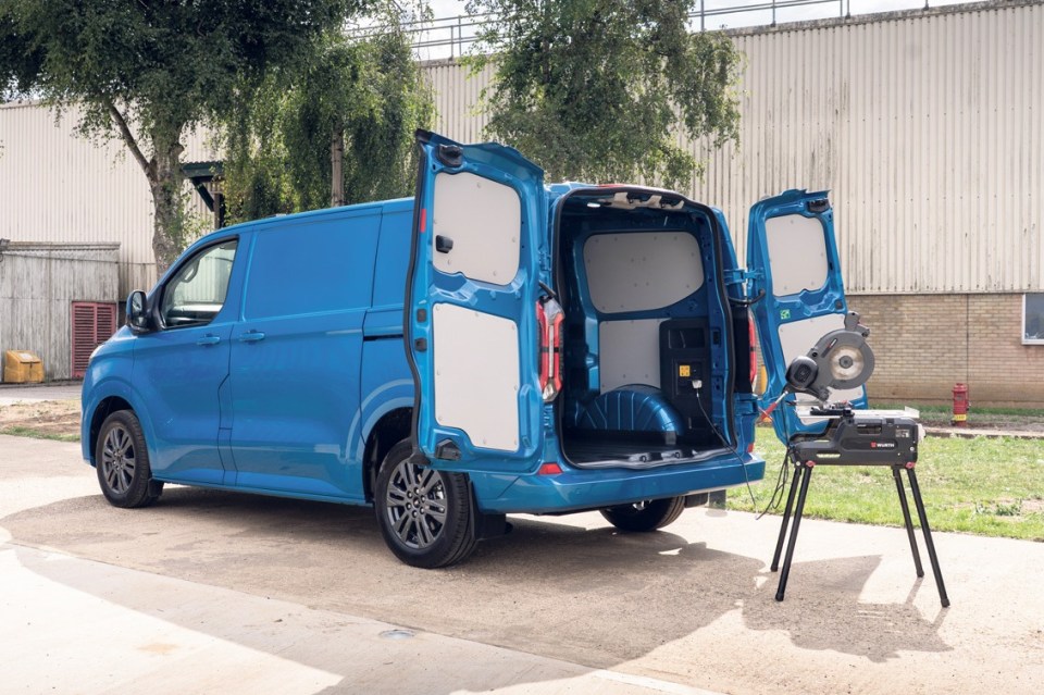 Blue van with its rear doors open, showing its empty cargo area; a miter saw sits outside the van.