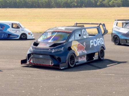 Five race vans and cars parked on a tarmac.