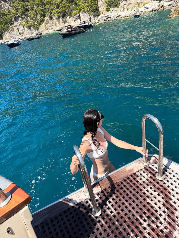 Woman in white bikini exiting the water onto a boat.