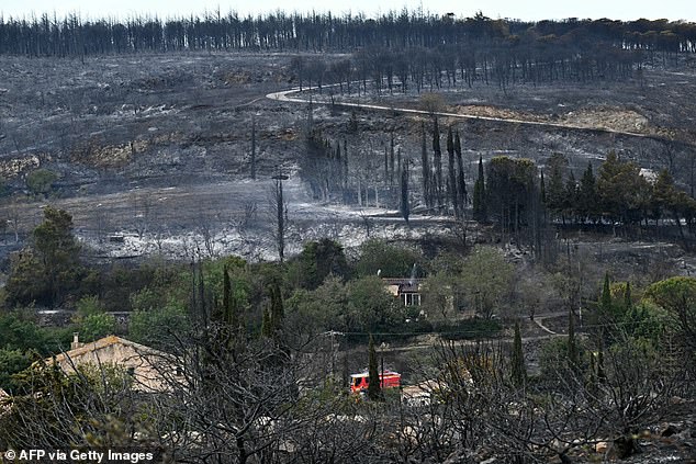 A firefighting vehicle drives past houses near an area devastated by a wildfire near Fontjoncouse, southwestern France