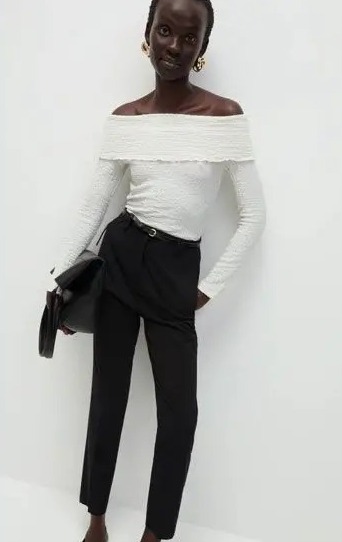 Model wearing a white off-the-shoulder top and black trousers.