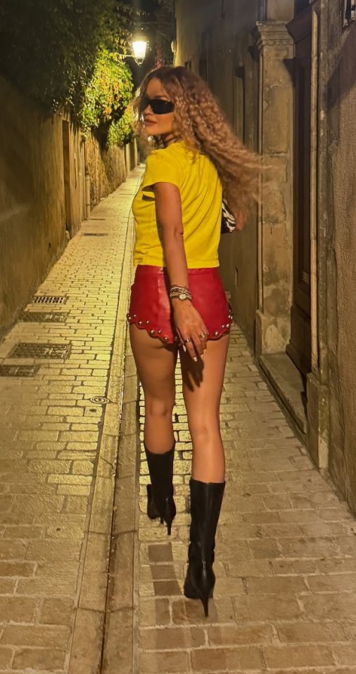 Rita Ora walking down a narrow street at night.