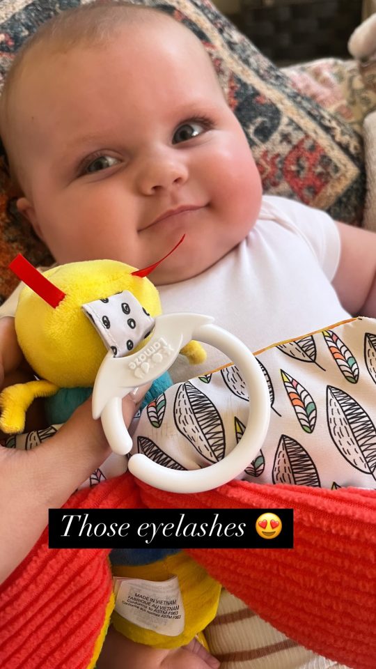 Close-up of a baby with long eyelashes holding a toy.