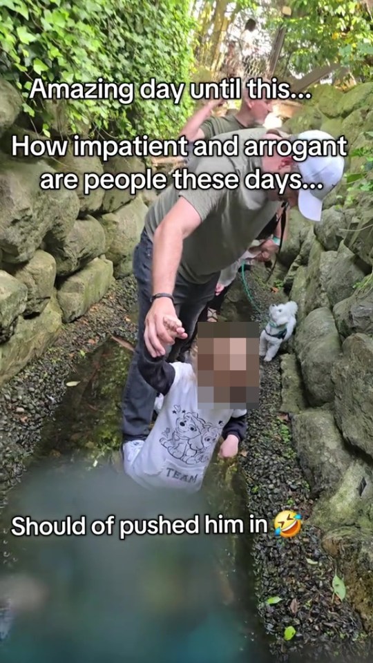 A child falls into a shallow stream while being helped by an adult.