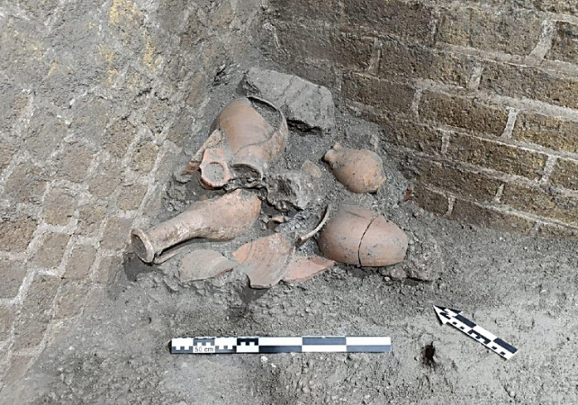 Archaeological excavation showing broken pottery fragments next to a brick wall.