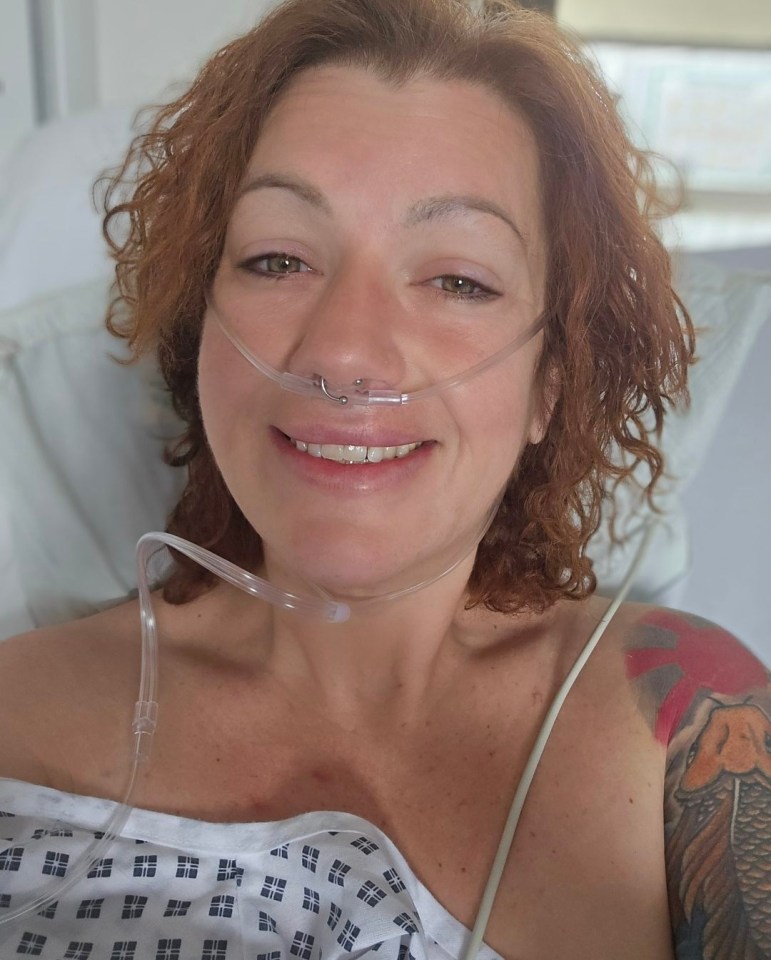 Woman in hospital gown smiling at camera with nasal cannula.