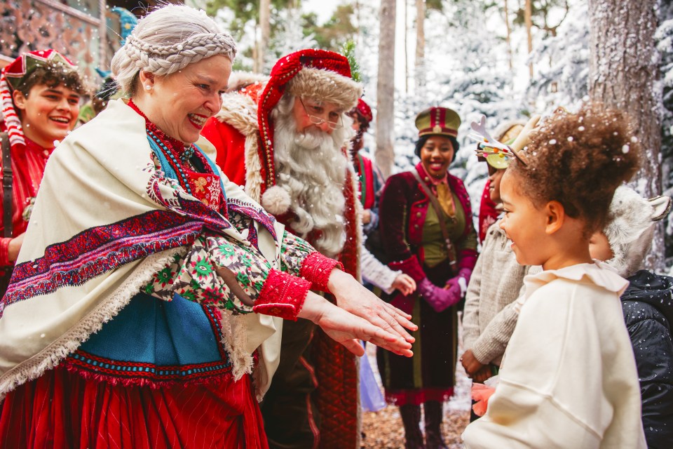 A woman in a traditional festive costume interacts with a child at a Lapland UK event.