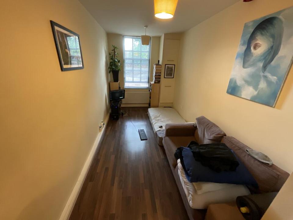 Narrow studio apartment with sofa, mattress, and small kitchen.