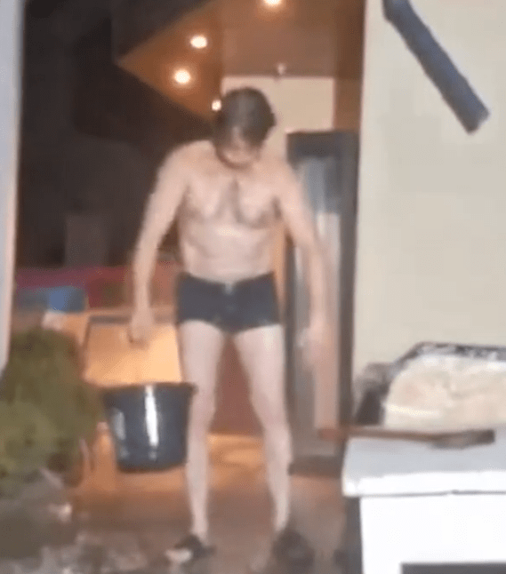 Shirtless man in shorts carrying a bucket.