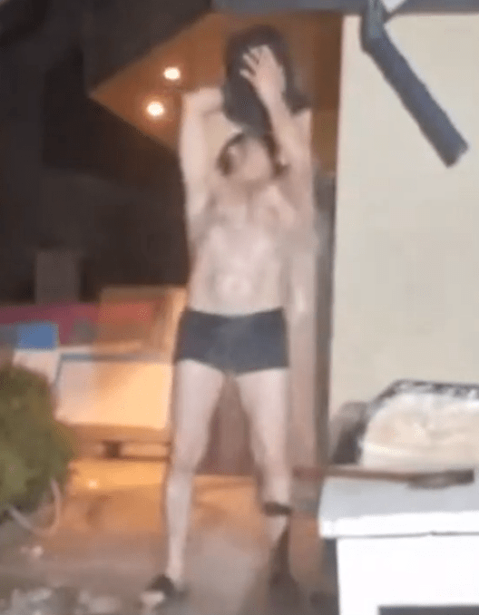 Shirtless man holding a shirt above his head.