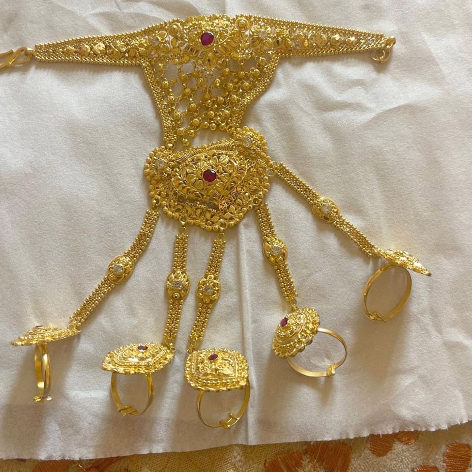Gold hand jewelry set with red and white stones.