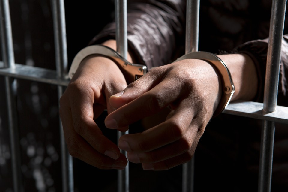 Handcuffed hands behind prison bars.