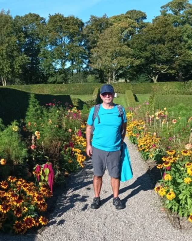 Man standing on a path between flowerbeds in a garden.