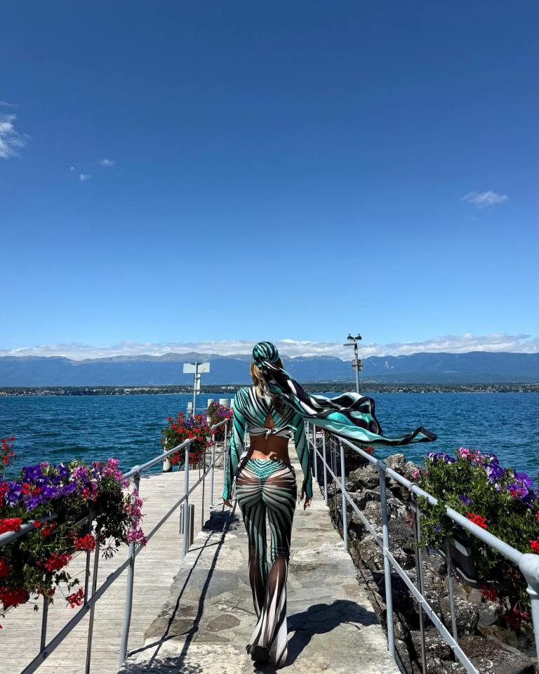 DAZN host Diletta Leotta in a teal and white striped bikini on a dock overlooking a lake and mountains.