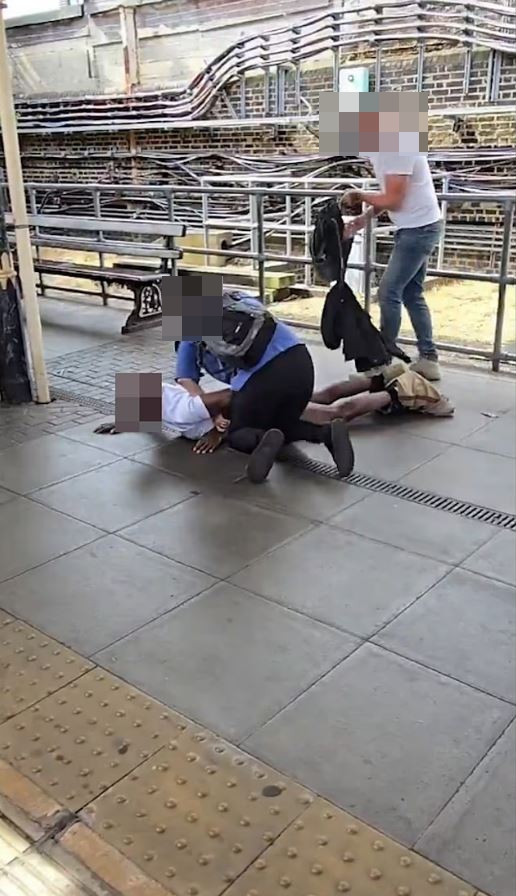 Passengers subduing a man on a train platform.
