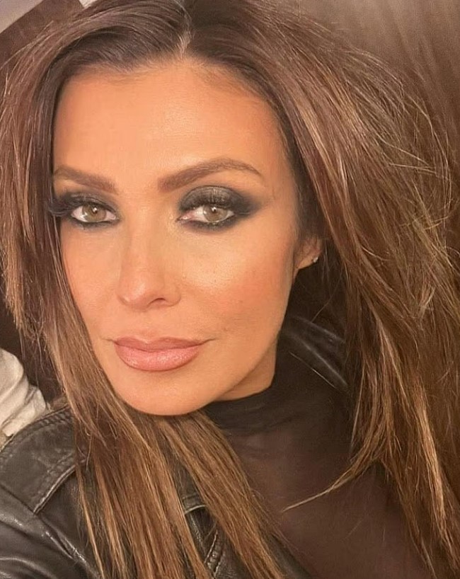 Close-up portrait of a woman with long brown hair and dark eye makeup.