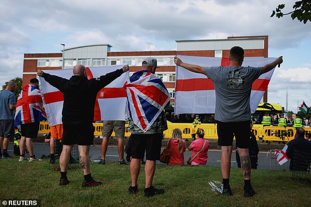 Anti-immigration demonstrators display Union Jack and England flags as they gather outside the Cresta Court hotel