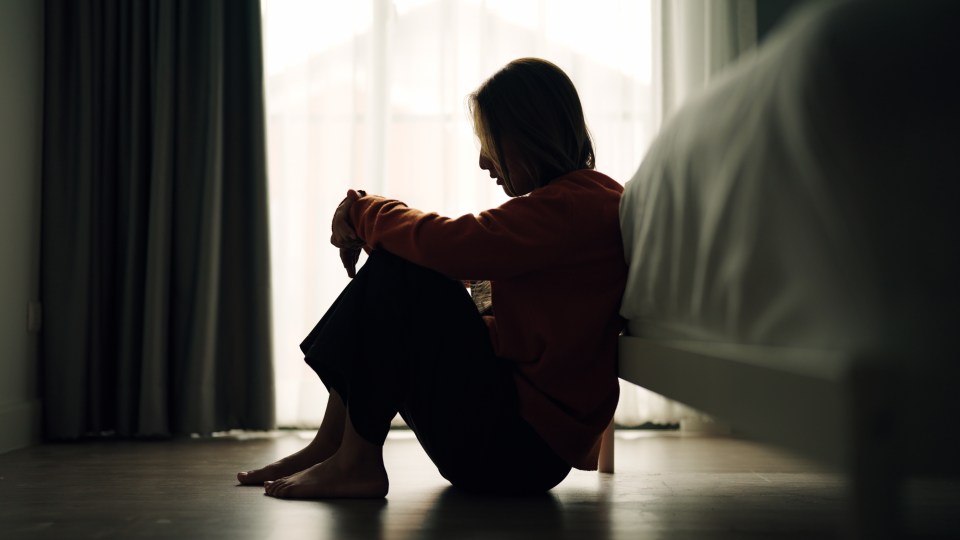 Silhouette of a sad woman sitting on the floor in a bedroom.