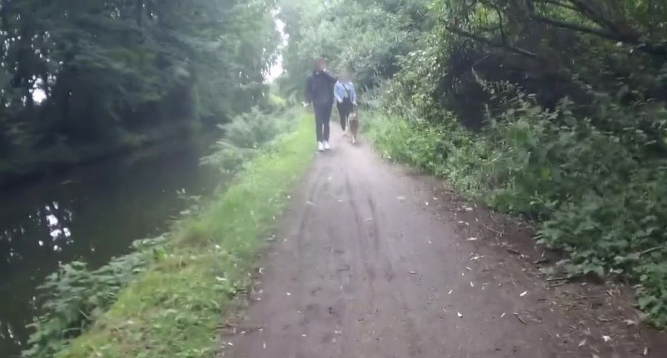 A couple walking a dog on a path beside a canal.