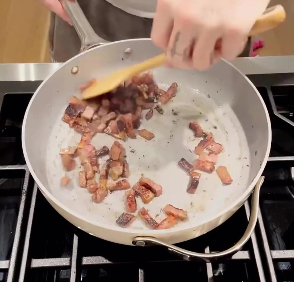 A person cooks bacon in a pan on a stovetop.