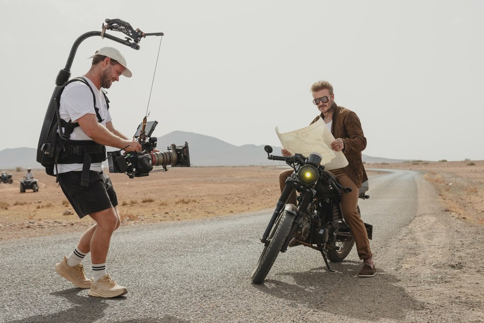 David Beckham on a motorcycle, looking at a map, being filmed.